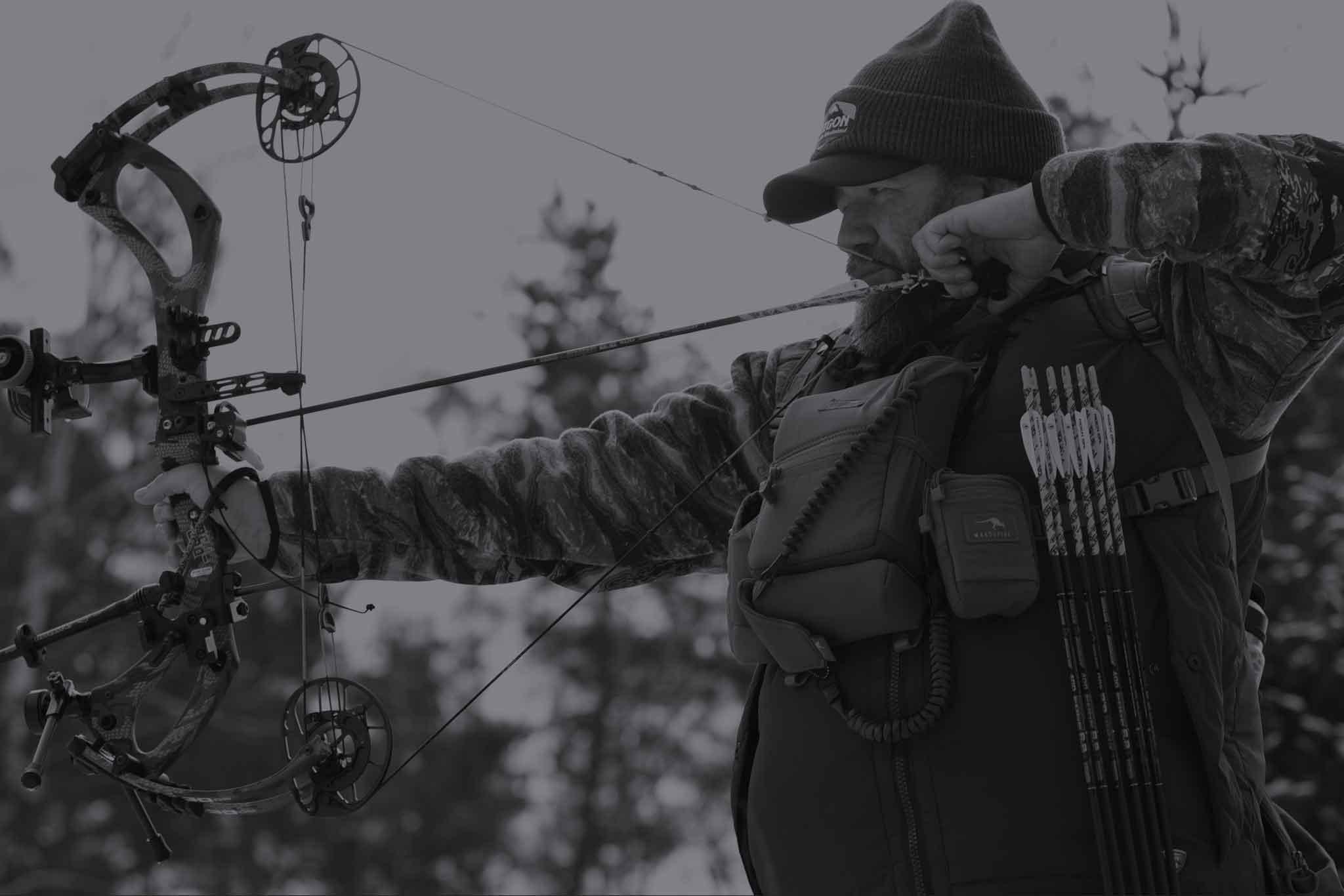 Bowhunter in camouflage drawing compound bow in forest